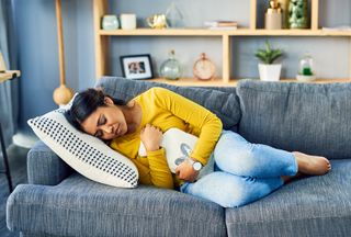 woman laying on sofa with hot water bottle on stomach