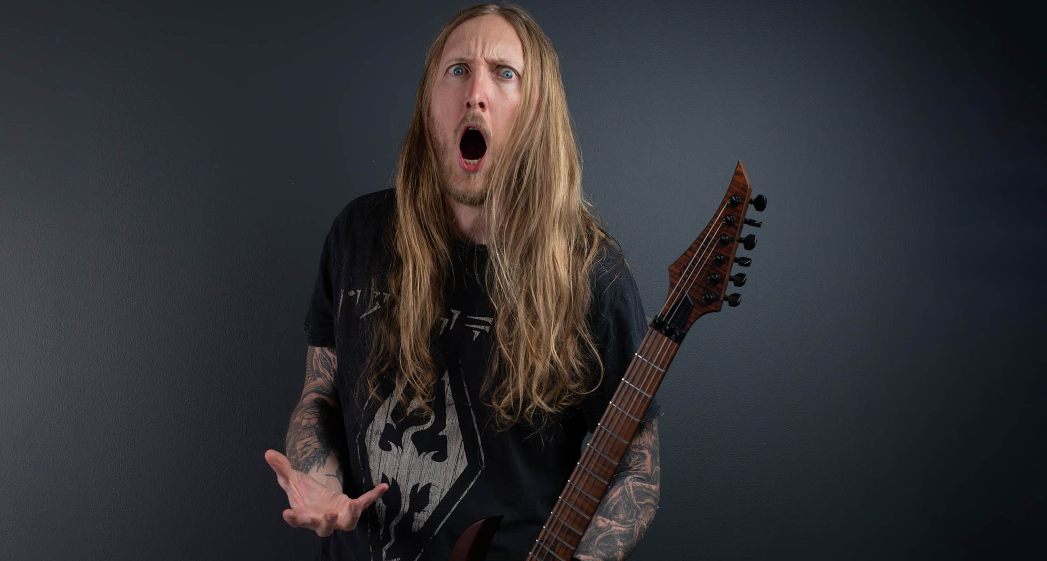 Ola England strikes a pose against a dark gray background. He holds one of his Solar Guitars