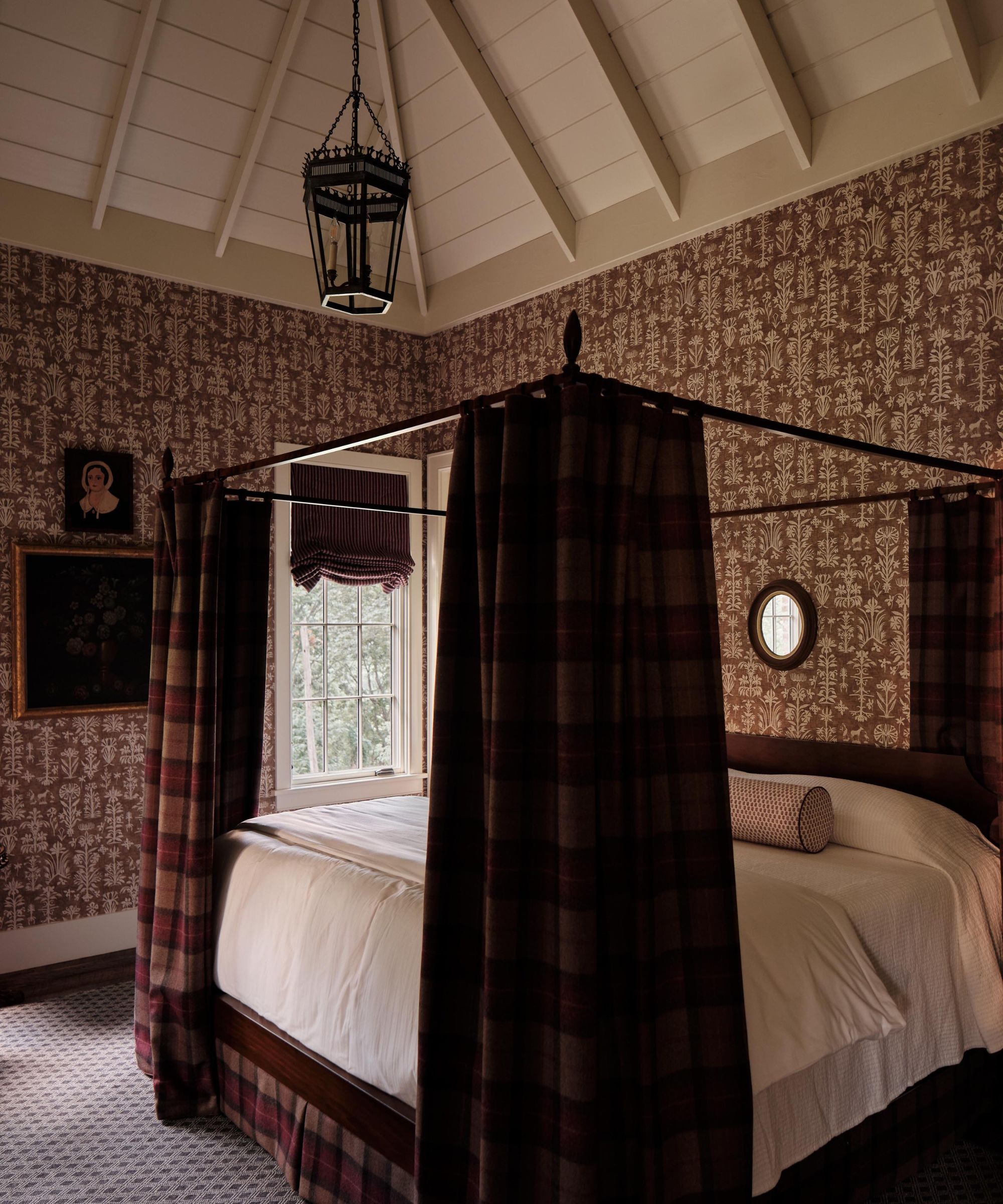 a cozy bedroom with red wallpapered walls, a four-poster bed with plaid bed curtains and white sheets, and a vaulted ceiling with a pendant hanging