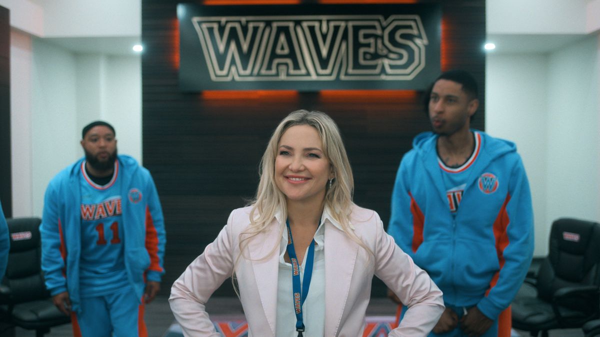 Isla Gordon smiles with her arms on her hips as two basketball players stand behind her in Running Point.