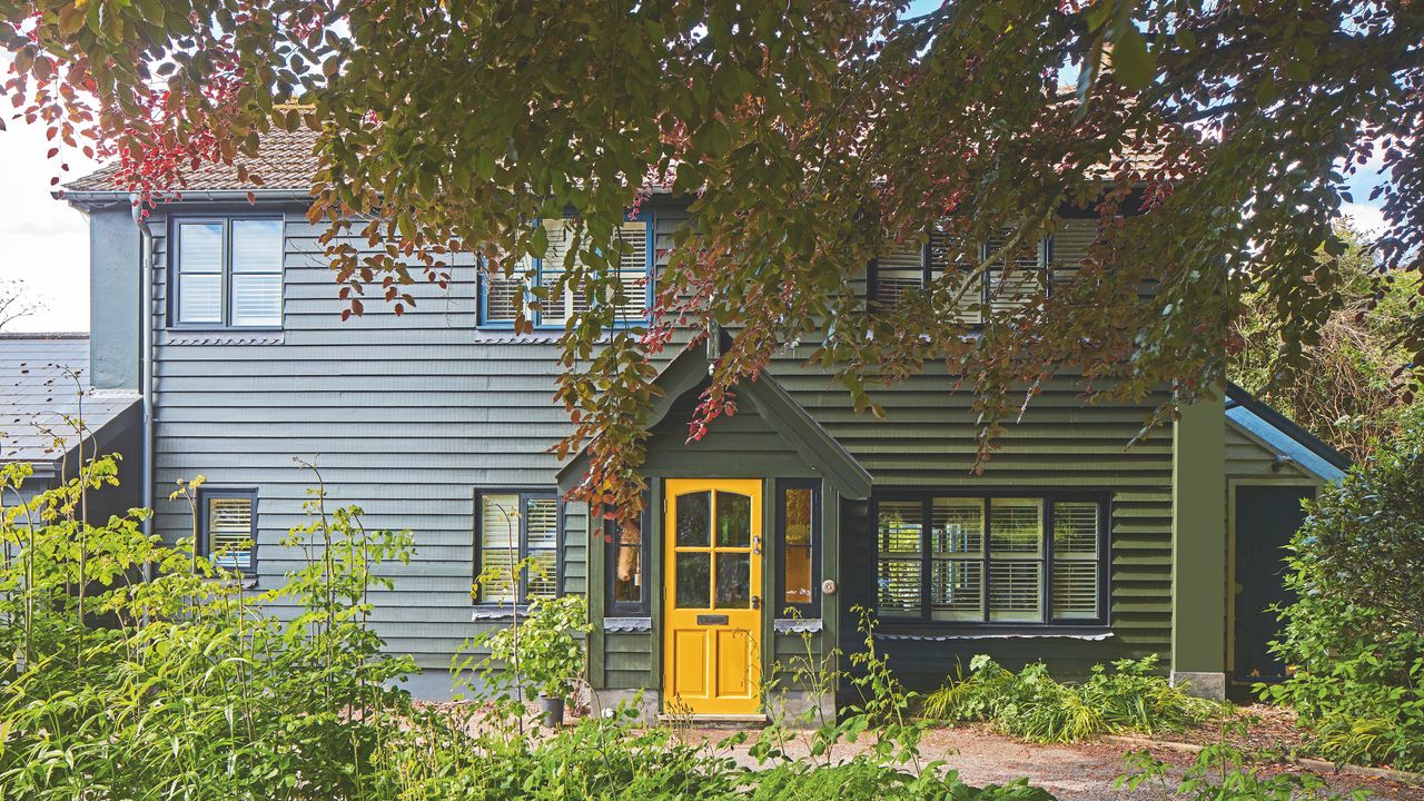 exterior of woodclad house painted dark olive green with yellow front door on porch