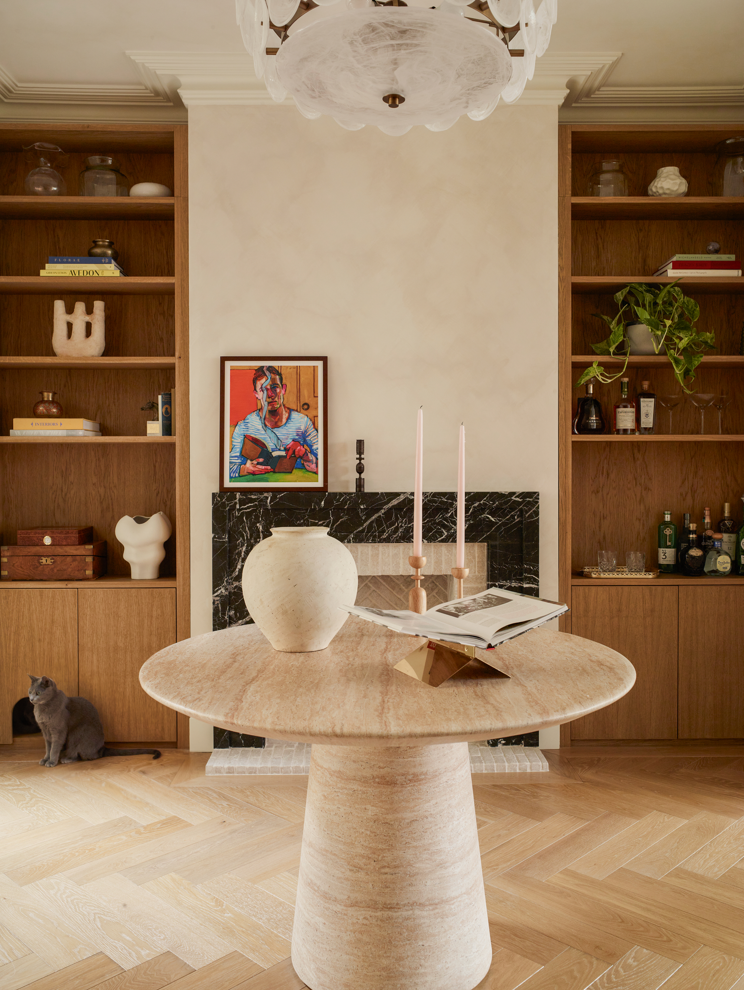 Snug space with beige walls, built-in wooden shelving in alcoves beside black marble fireplace, and round travertine table