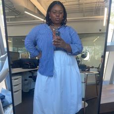 chichi wears blue striped button down and white skirt while taking a mirror selfie in theBest Knockoff Luxury Clothing
 offices