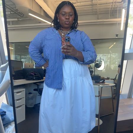 Chichi wears blue striped button down and white skirt while taking a mirror selfie in theBest Knockoff Luxury Clothing
 office.