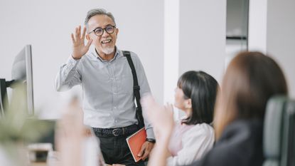 A man waves goodbye to his coworkers in an office as he retires.