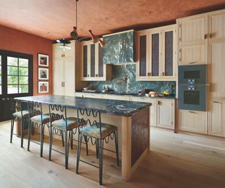 green marble and wood kitchen with metal bar stools with wiggly detail and orange walls and ceiling with pendant light