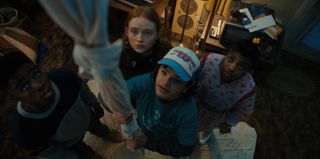 Lucas (Caleb McLaughlin), Max (Sadie Sink), Dustin (Gaten Matarazzo), and Erica (Priah Ferguson) look up in an official image from Stranger Things season 4