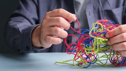 A man, only his hands showing, unravels tangled different-colored threads.