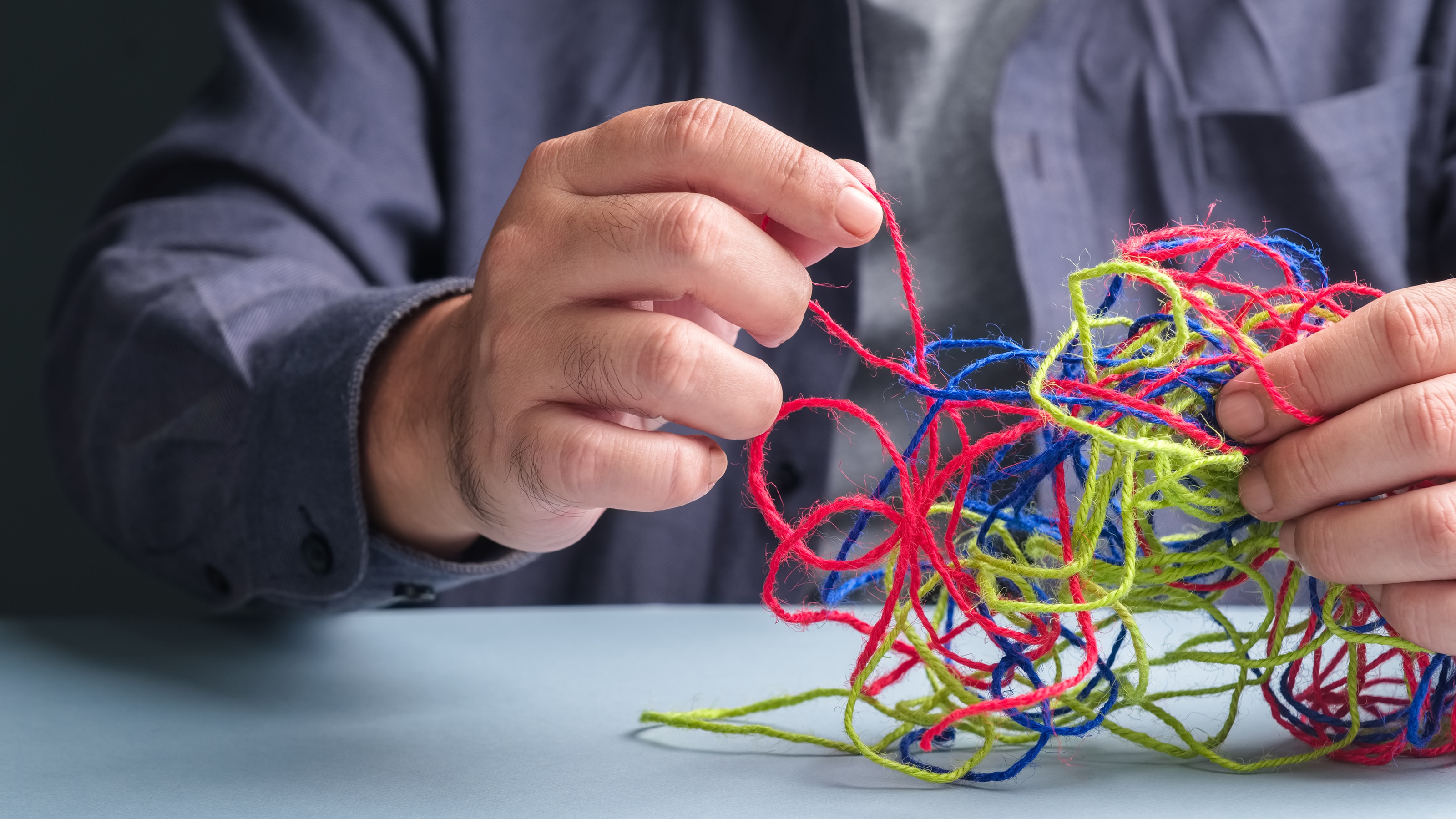 A man, only his hands showing, unravels tangled different-colored threads.