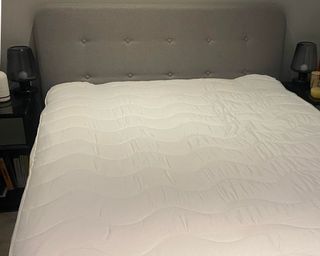 Pillow on a mattress on Louises bed with grey headboard