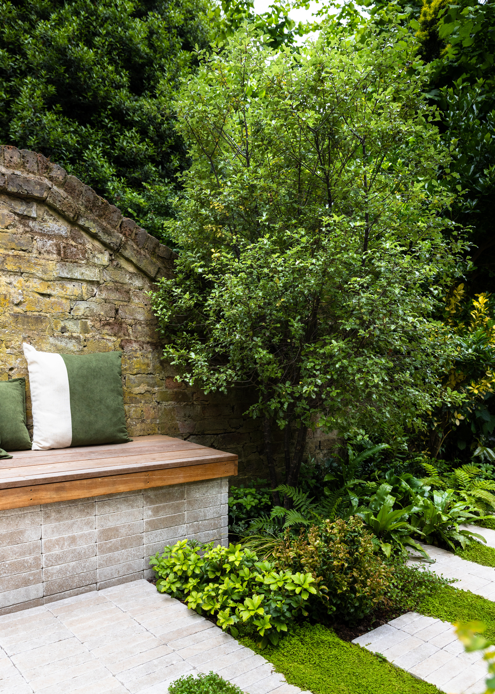 a reclaimed brick wall behind a built-in bench with green and white cushions in a garden