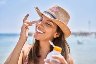 A woman in a sun hat applying sun cream to her face
