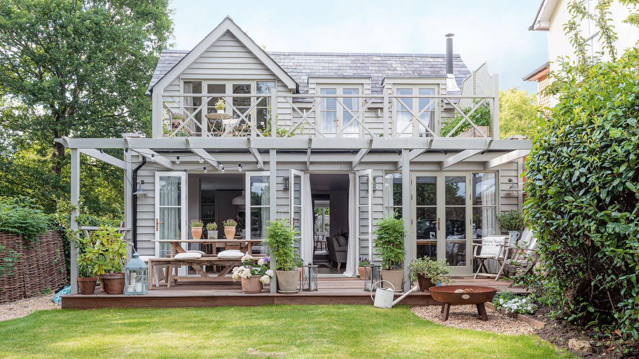 exterior of gray painted timber clad converted coach house with decking and trees around