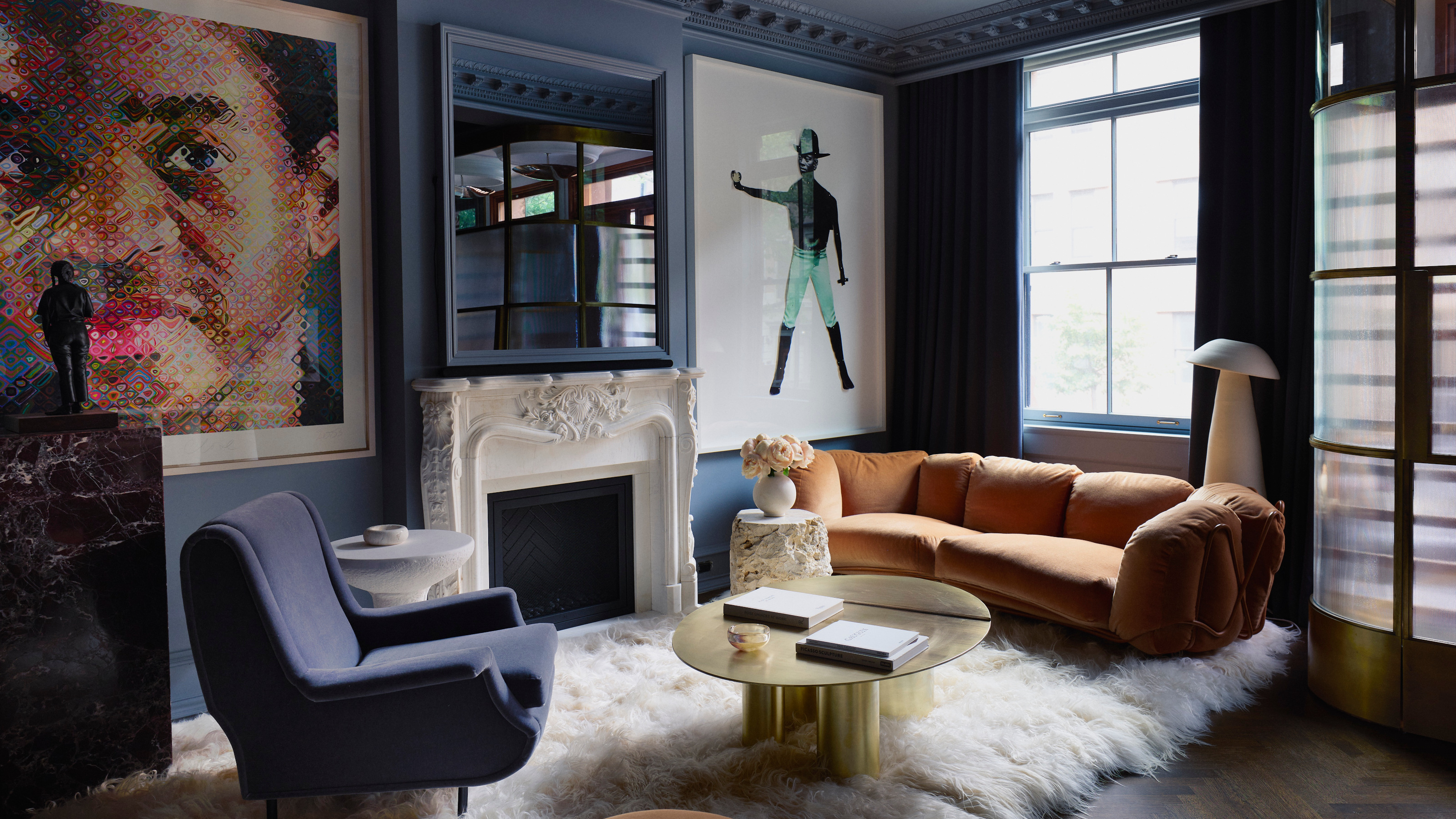 Navy living room with orange curved sofa, navy armchair, large figurative artwork, brass round coffee table, fluffy cream rug and white floor lamp