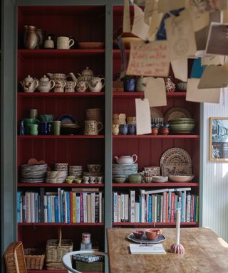 dining room with bookcase and shelving for display, tableware, baskets, hanging display, candle, red bookcase, grey walls