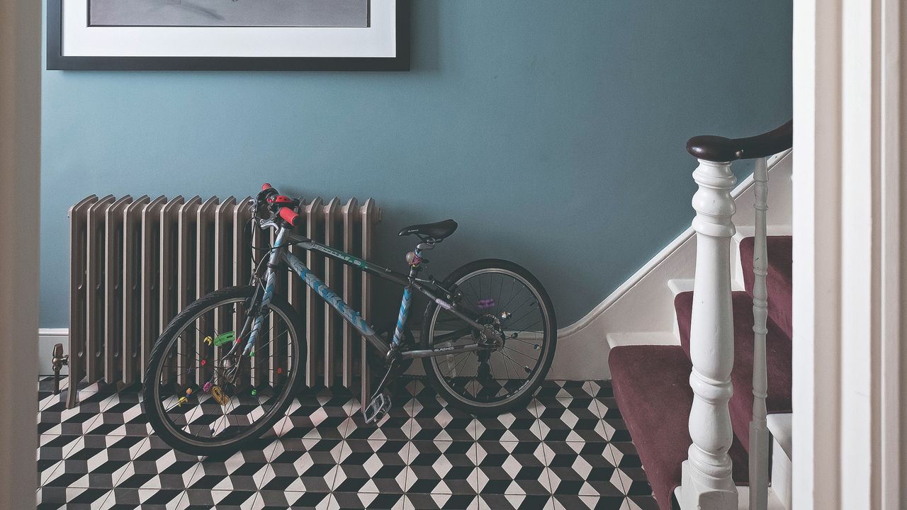 Blue-painted hallway with a black radiator, a child&#039;s bicycle and a geometric-tiled floor