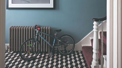 A blue-painted hallway with a black radiator, a child's bicycle and geometric tiles