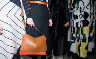 Female models wearing navy and patterned clothes, holding a tan and orange handbag from the Jil Sander A/W 2015 collection