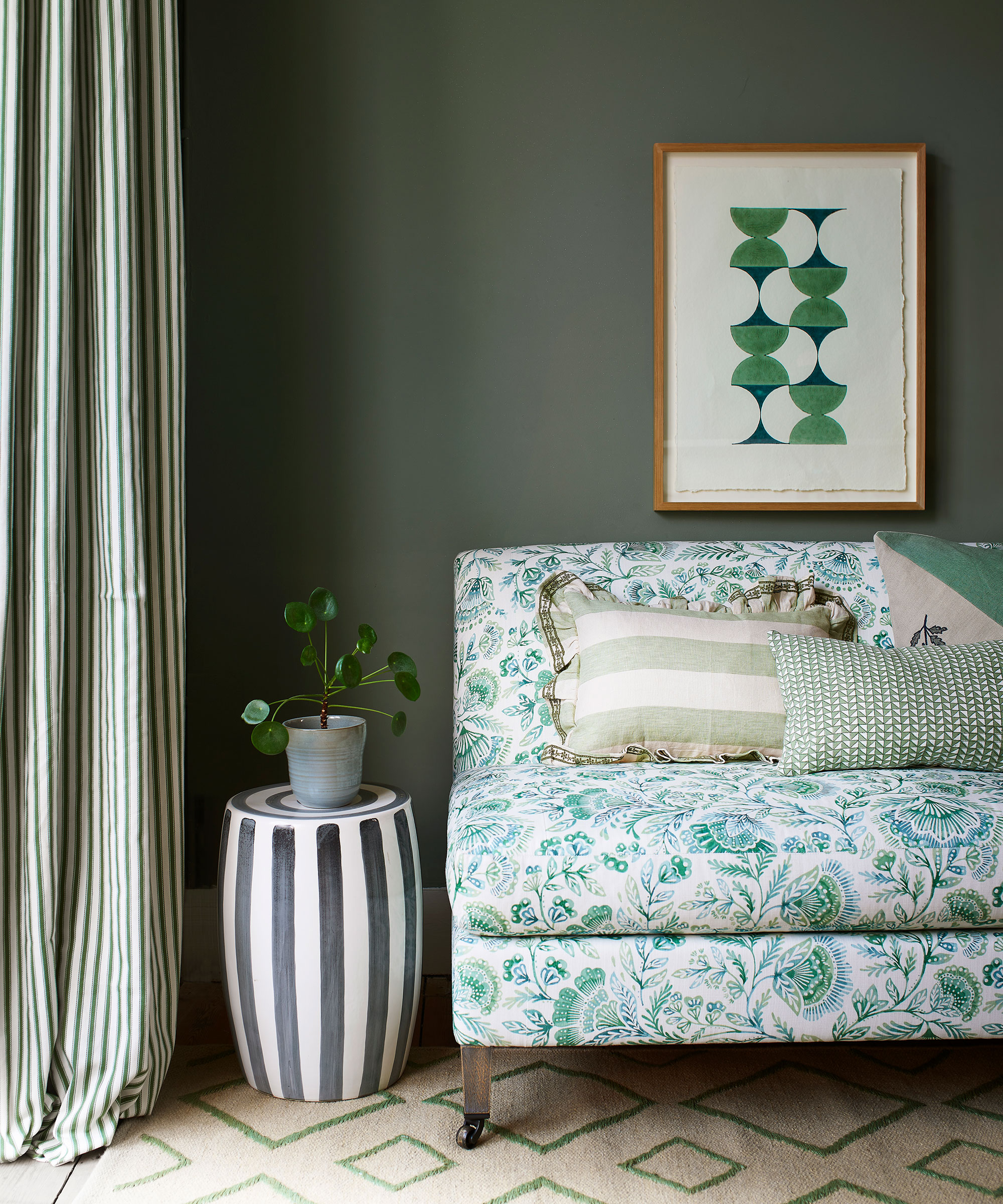 green painted living room with botanical print sofa and stripy drum side table