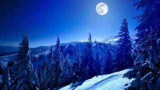 A full moon shines over a snowy mountain.