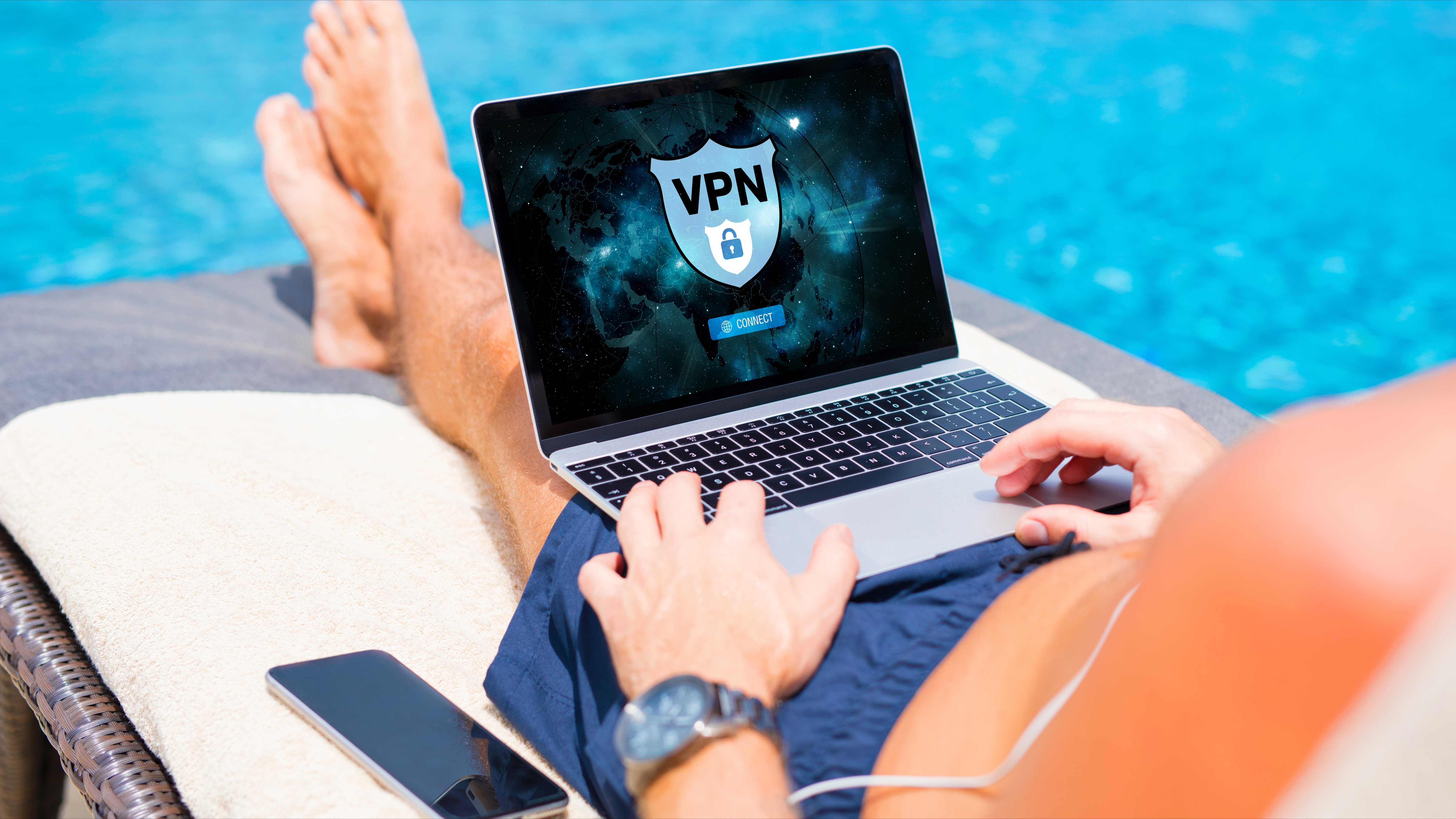 A man loads a VPN on his laptop while reclining on a deck chair by the pool.