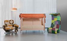 Lounge chair in the beige, brow, and orange geometrical shapes upholstery, a two-seater sofa in pale pink and orange, and a highback chair in purple, yellow, red, and various shades of green upholstery.