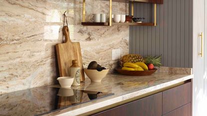 Natural stone worktop with a black electric cook top. A bowl of fruit in the corner and a wooden cutting board leaning against the wall. 