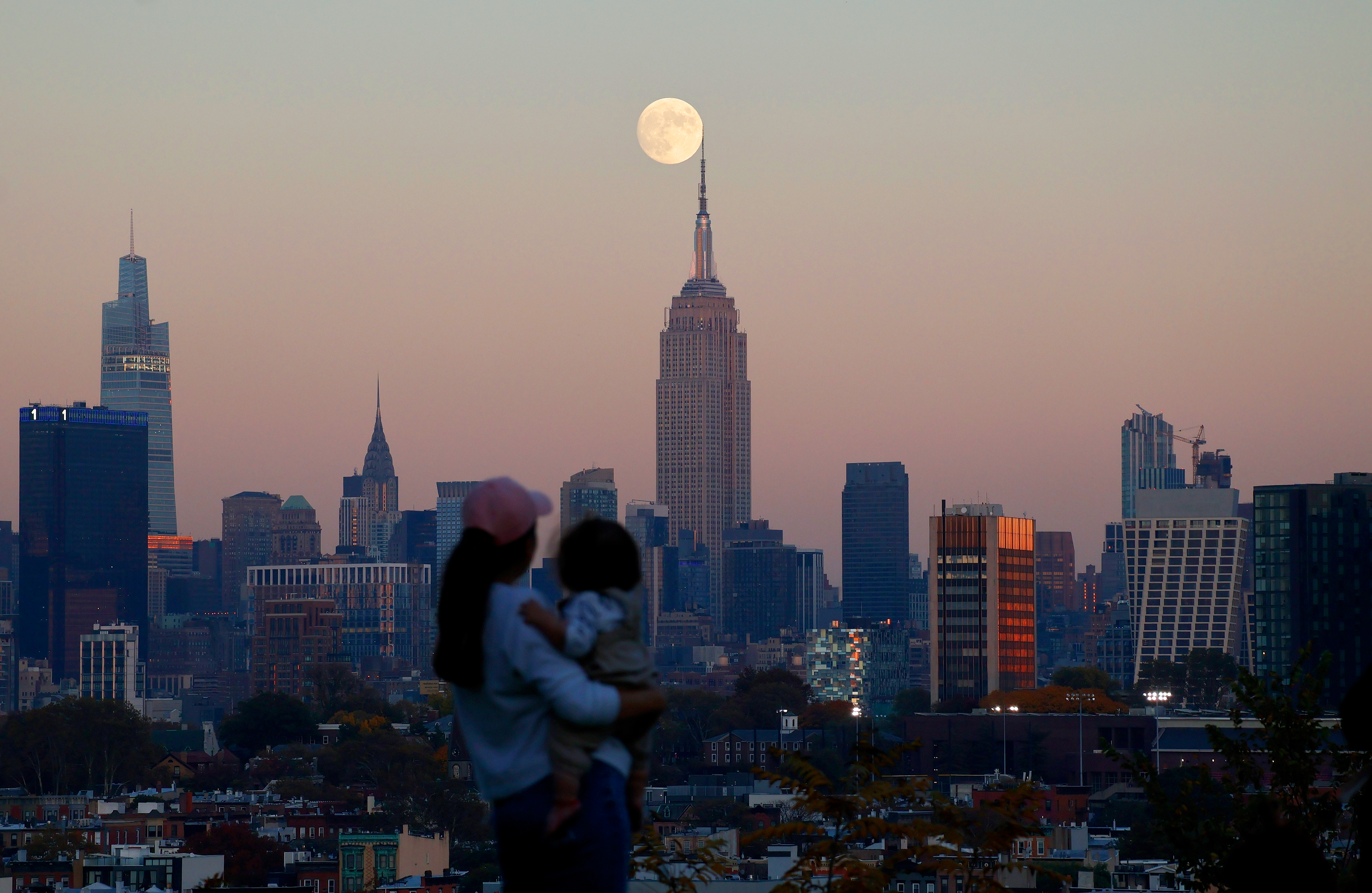 A large full moon hovers directly above the Empire State Building in a scene of the New York skyline.