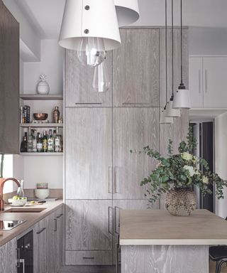 Kitchen diner with pale grey wood cabinets, wooden floor and white lamps over the kitchen island and white walls