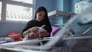 A mother sits on a hospital bed in Kuala Lumpur, Malaysia, with her newborn baby in her arms