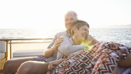 An older couple smile and cuddle on a boat.