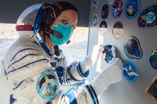 NASA astronaut Kate Rubins affixes an Expedition 64 decal inside the bus carrying her and fellow crewmates Russian cosmonauts Sergey Kud-Sverchkov and Sergey Ryzhikov of Roscosmos to the launch pad at the Baikonur Cosmodrome in Kazakhstan on Oct. 14, 2020.