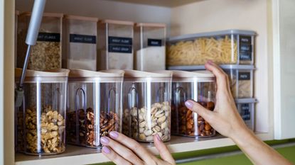 Organizing a cupboard with clear containers filled with nuts and other dry goods such as pasta