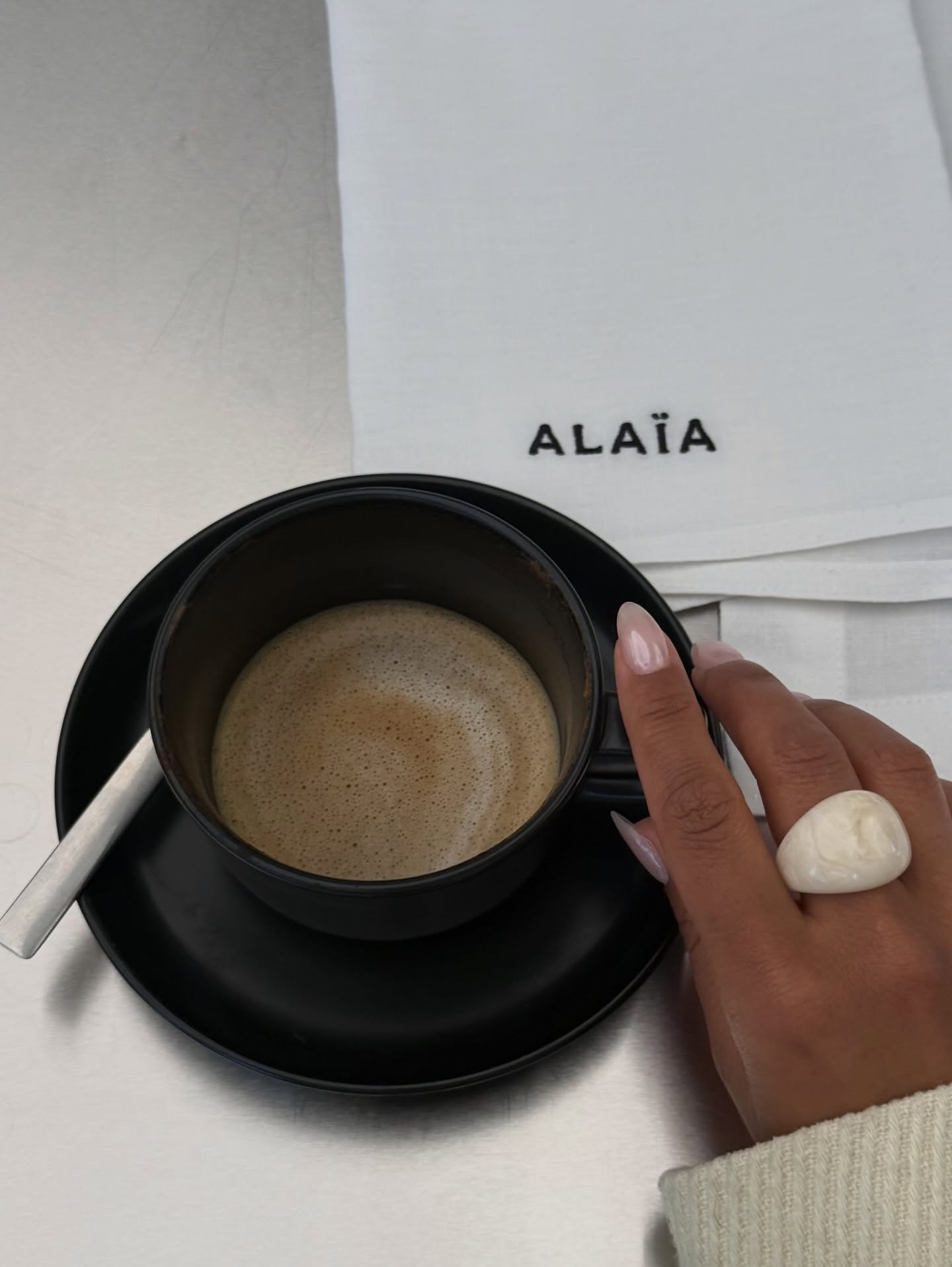 A woman holding a coffee cup with a chrome manicure wearing a chunky ring