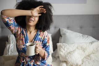 Exhaustion symptoms: African American woman sitting in bed drinking coffee