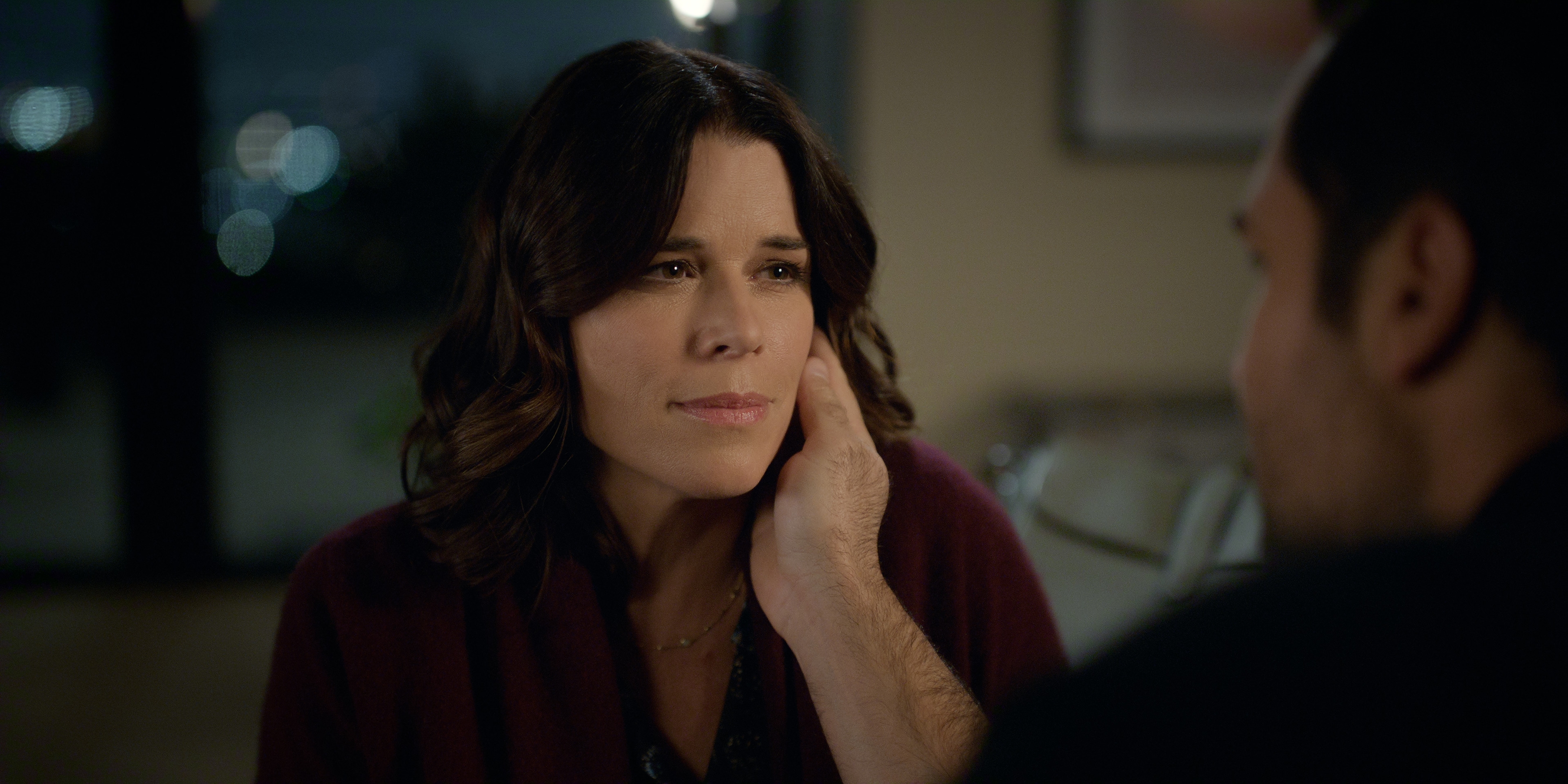 Neve Campbell as Maggie in episode 408 of The Lincoln Lawyer wearing a red top as a man caresses her face