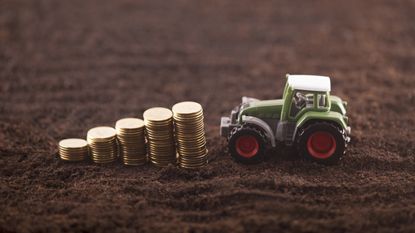 A stack of coins next to a toy tractor sitting on a layer of dirt.