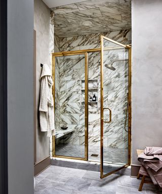 Double door shower enclosure with marbled tiles, recessed shelving, gown hanging and stool in corner