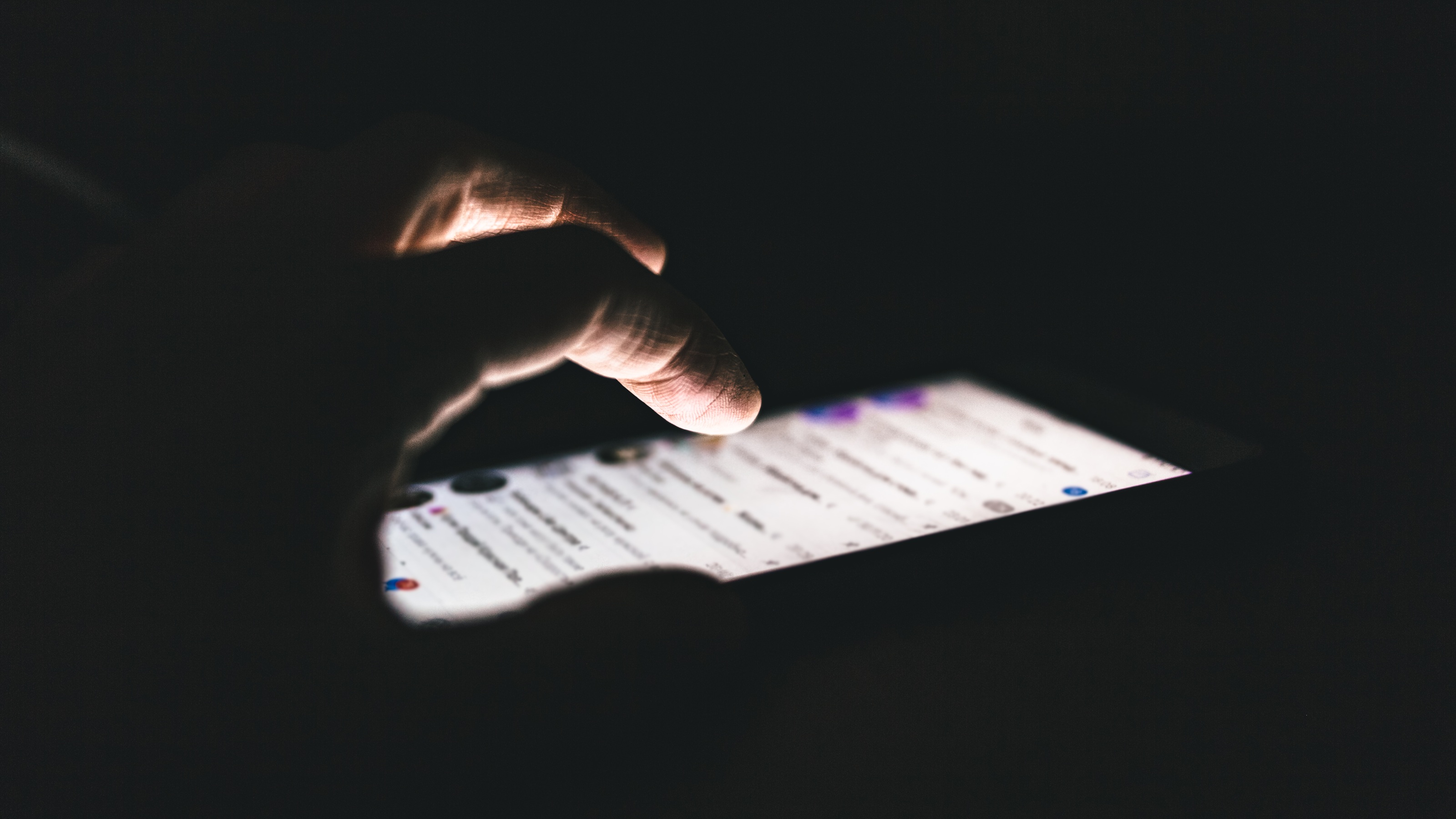 A person looks at their social media, only their hand and the phone screen showing in the dark.