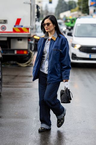 A guest wears Miu Miu blue jacket, striped jeans, black bag outside Magliano during the Milan Fashion Week Menswear Fall/Winter 2025-2026