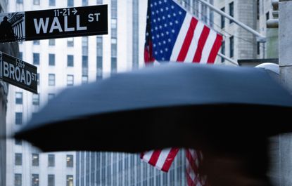 Private credit concept: A pedestrian carrying an umbrella passes a U.S. flag on Wall Street in New York
