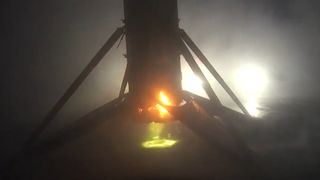 a charred rocket stands upright on a flat barge lit by lights in early morning fog