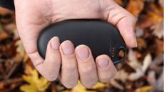 best hand warmers: Black Lifesystems reusable hand warmer in someone's hand, against backdrop of autumn leaves