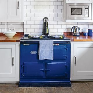 kitchen with white brick tiles wall blue aga and white cabinet wooden worktop