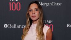 Image of Victoria Beckham looking at the camera with long blonde wavy hair and wearing a light pink dress