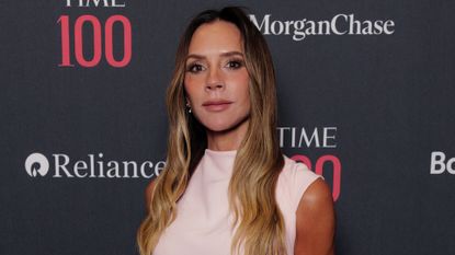 Image of Victoria Beckham looking at the camera with long blonde wavy hair and wearing a light pink dress