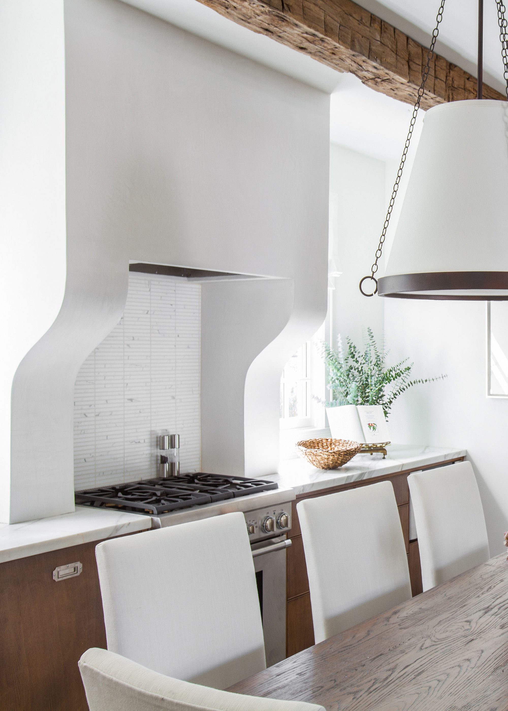 A white kitchen with a plastered-in range hood and a dining table with chairs in the middle