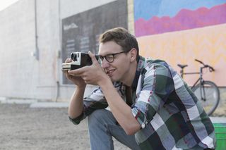 A photographer, kneeling down, taking a photograph with a Polaroid camera