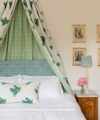 Moly Mahon bedroom with canopy over bed in pretty floral/botanical print, lined with green check, matching cushion, small bedside, pictures on wall