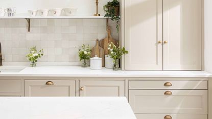 A neutral ktichen with brass cabinet and drawer handles, a marble splashback